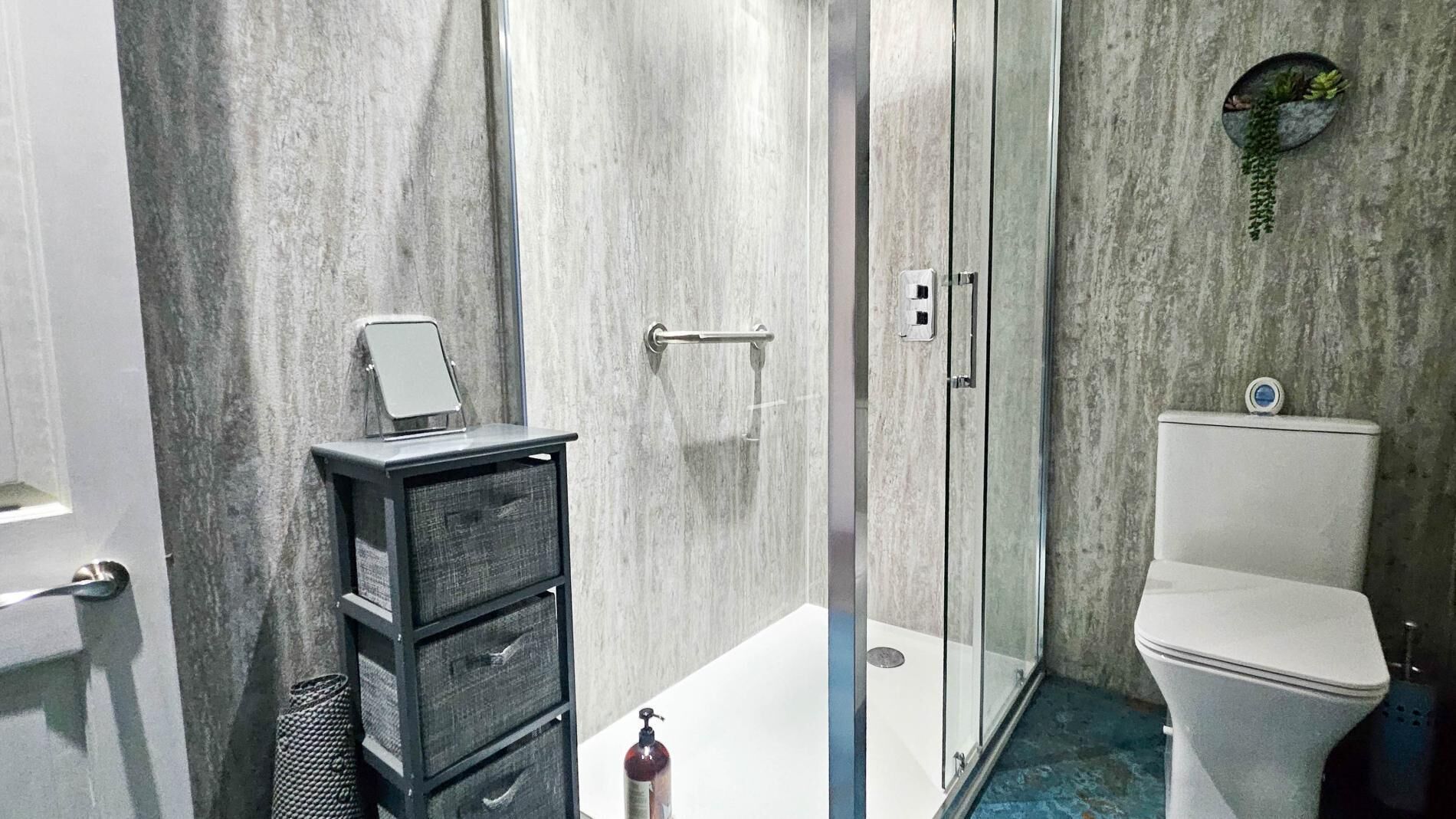A modern bathroom with a glass shower enclosure, a white toilet, and a small black storage unit with drawers.