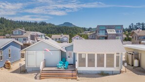 A beachfront property with a covered patio, outdoor seating, and a view of the forested hills.