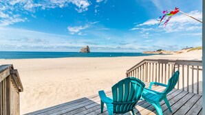A beach view with a wooden deck, two turquoise chairs, and a colorful kite flying.
