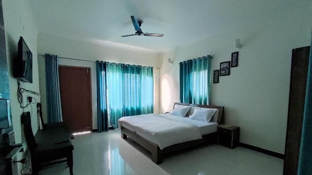 A bedroom with a bed, a desk, a chair, a TV, and curtains. - Valley View Inn (Nainital)