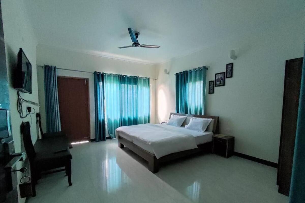 Un dormitorio con cama, escritorio, silla, televisor y cortinas.