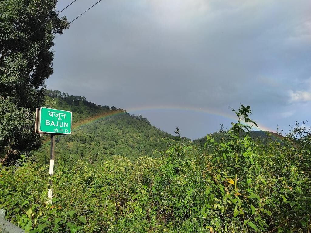 A sign for Bajun with a lush green landscape and a rainbow in the background.