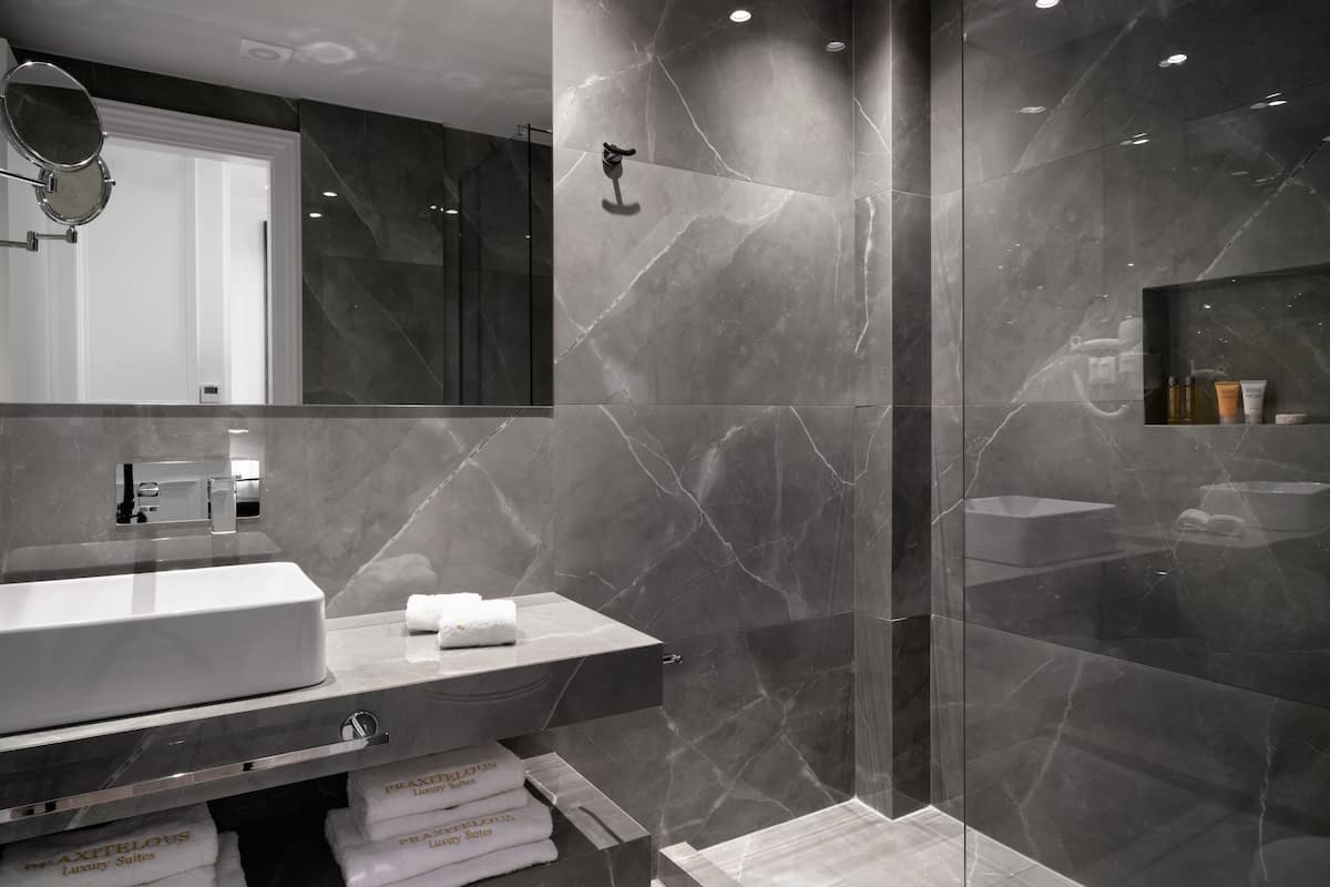 Un baño moderno con tocador de mármol, cabina de ducha de vidrio y repisa con artículos de aseo.