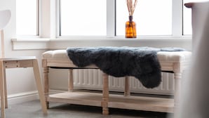 A room with a wooden bench, a radiator, and a window with a vase of dried plants. - Marlborough Court - Donnini Apartments (Ayr)
