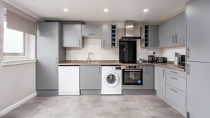 A modern kitchen with grey cabinets, a dishwasher, a washing machine, and a stove. - Marlborough Court - Donnini Apartments (Ayr)