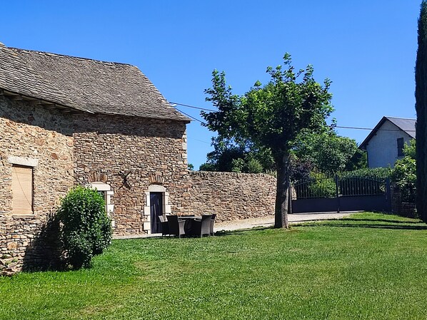 A stone building with a tiled roof, a small door, and a window. There is a tree in front of the building and a grassy lawn. - Ancienne Bergerie Rénovée , Proche des Lacs, Sentiers Pédestres (COMPS LA GRANDVILLE)