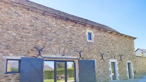 Un bâtiment en pierre avec une allée gravillonnée et deux grandes portes en bois.