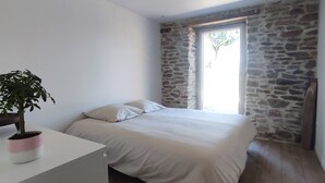 Une chambre à coucher avec un lit, une plante en pot, une fenêtre donnant sur un paysage et un mur en pierre.