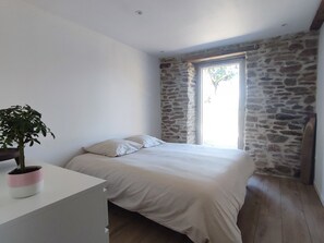 Quarto com cama, planta em vaso, janela com vista e parede de pedra.