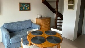 Un soggiorno con un divano blu, un tavolo da pranzo in legno con quattro sedie, una scala e un armadio in legno.