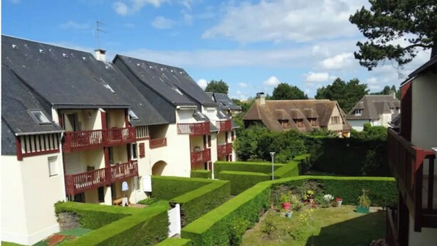 Una zona residenziale con diverse case, ciascuna con tetto a falde e un balcone. Le case sono circondate da giardini curati, con siepi e prati.