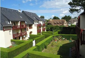 A residential area with multiple houses, each with a sloped roof and a balcony. The houses are surrounded by well-maintained gardens with hedges and lawns.