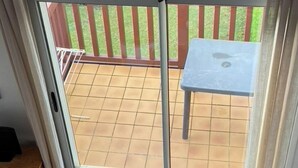 Una stanza con una porta scorrevole in vetro che si apre su un patio esterno con pavimento piastrellato e un tavolino.