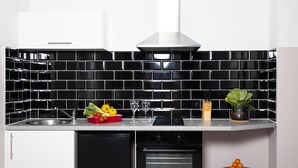 Une cuisine moderne avec un dosseret de carreaux noirs, des appareils en acier inoxydable et un tabouret bleu orné de motifs orange.