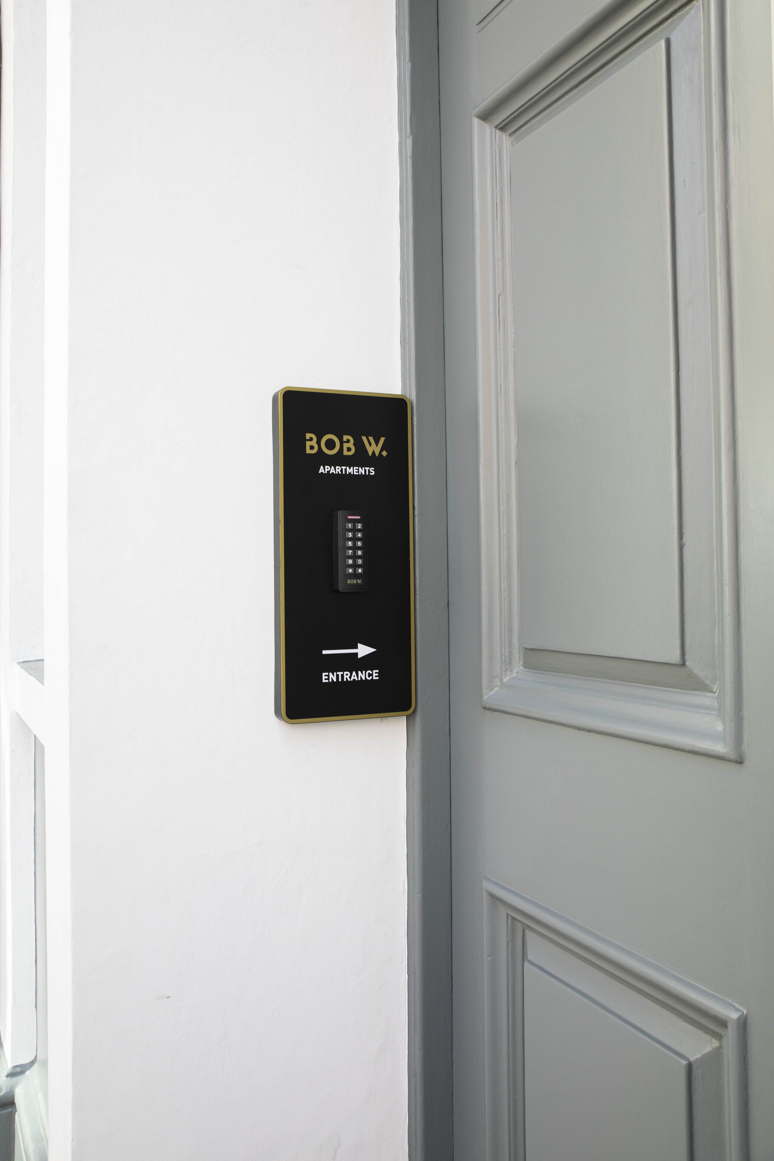 A wall-mounted electronic keypad with "BOB W. APARTMENTS" and "ENTRANCE" labels, indicating a secure entry point for a residential building.