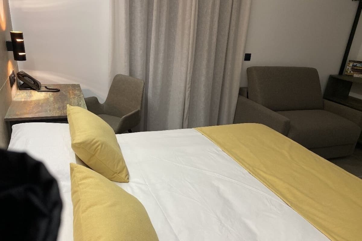 A hotel room with a bed, two armchairs, a nightstand with a phone, and a curtain.
