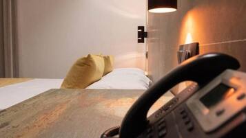 A hotel room with a bed, a bedside table, a telephone, and a wall-mounted light fixture.