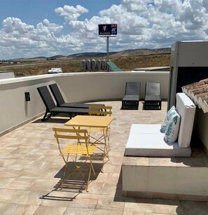 Una terraza en la azotea con una mesa, sillas, un sofá y un colchón.