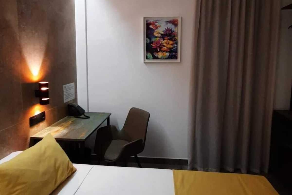 A hotel room with a bed, a desk, a chair, a painting, and a curtain.