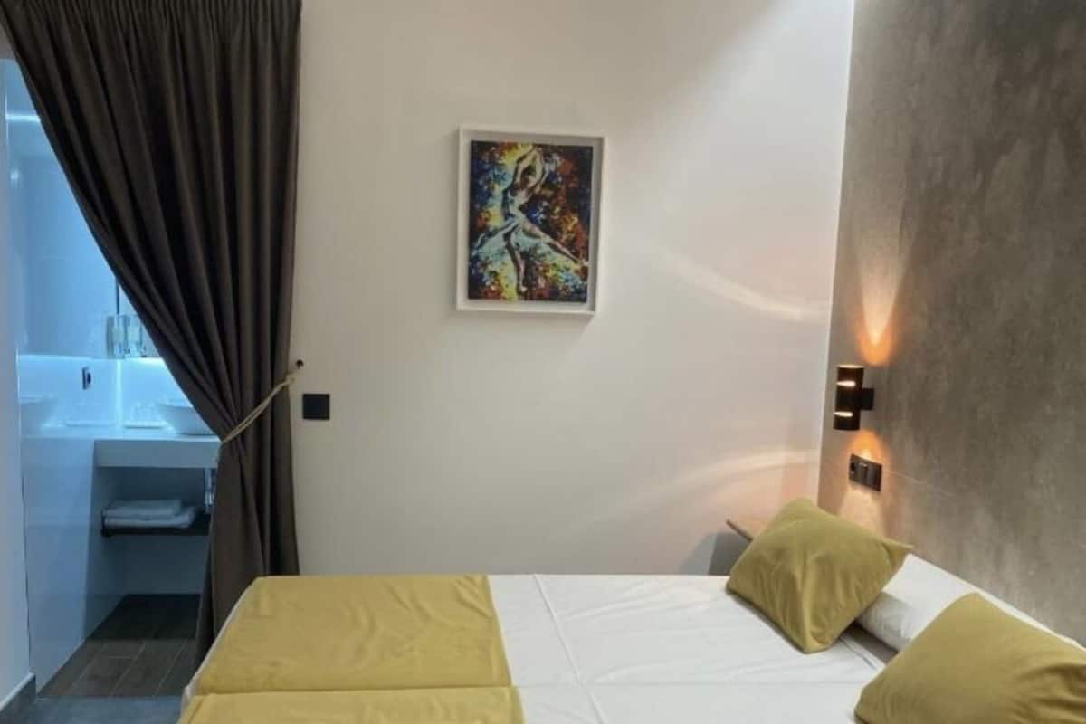 A hotel room with a bed, a painting on the wall, a bathroom with a sink, and a shower area.