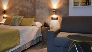 A hotel room with two beds, a sofa, a small table, and wall-mounted lamps.