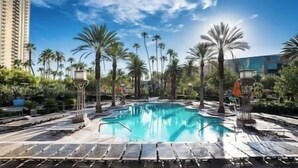 Une piscine entourée de palmiers et de chaises longues, avec un ciel bleu clair en arrière-plan.