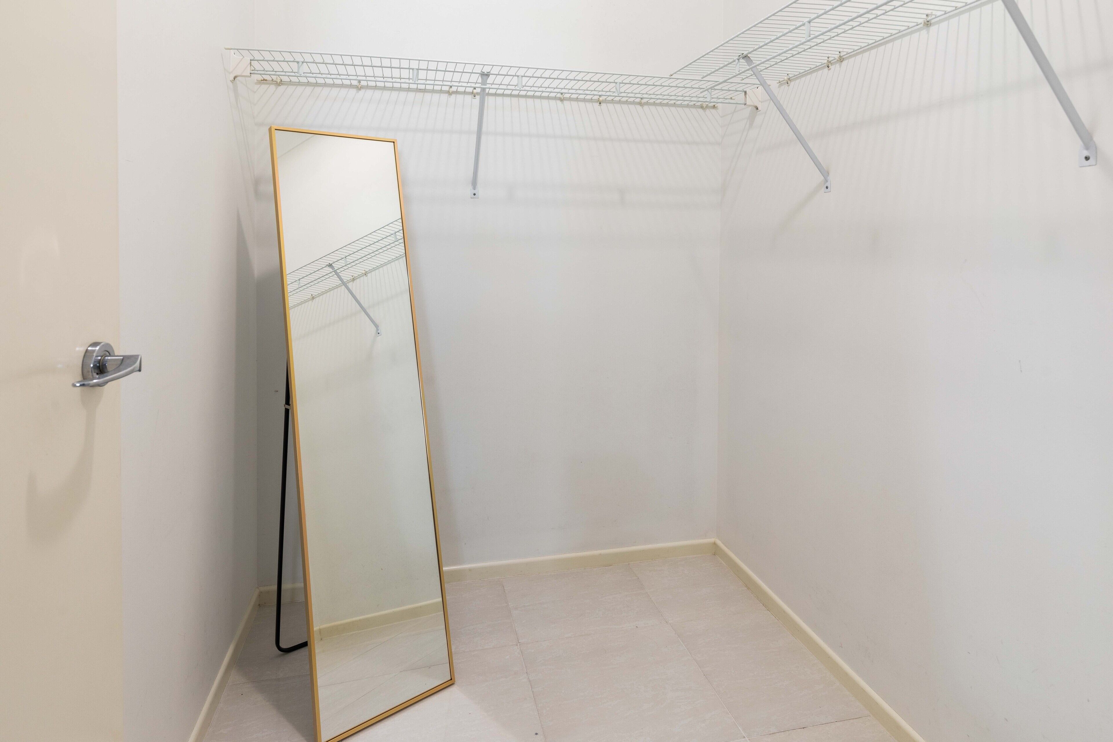 Un vestidor con espejo de cuerpo entero, estantería metálica y suelo de baldosas.