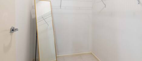 Un vestidor con espejo de cuerpo entero, estantería metálica y suelo de baldosas.