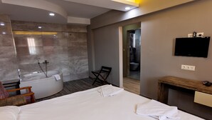 Ein modernes Hotelzimmer mit einem großen Bett, einer Badewanne, einem Holzstuhl, einem kleinen Tisch und einem an der Wand befestigten Fernseher.