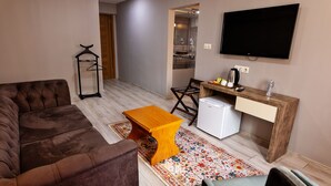 Ein Wohnzimmer mit einer braunen Couch, einem Holztisch, einem kleinen Fernseher und einem Kühlschrank.