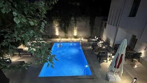 Ein rechteckiger Pool mit gefliestem Sonnendeck, umgeben von Liegestühlen und einem Coca-Cola Sonnenschirm.