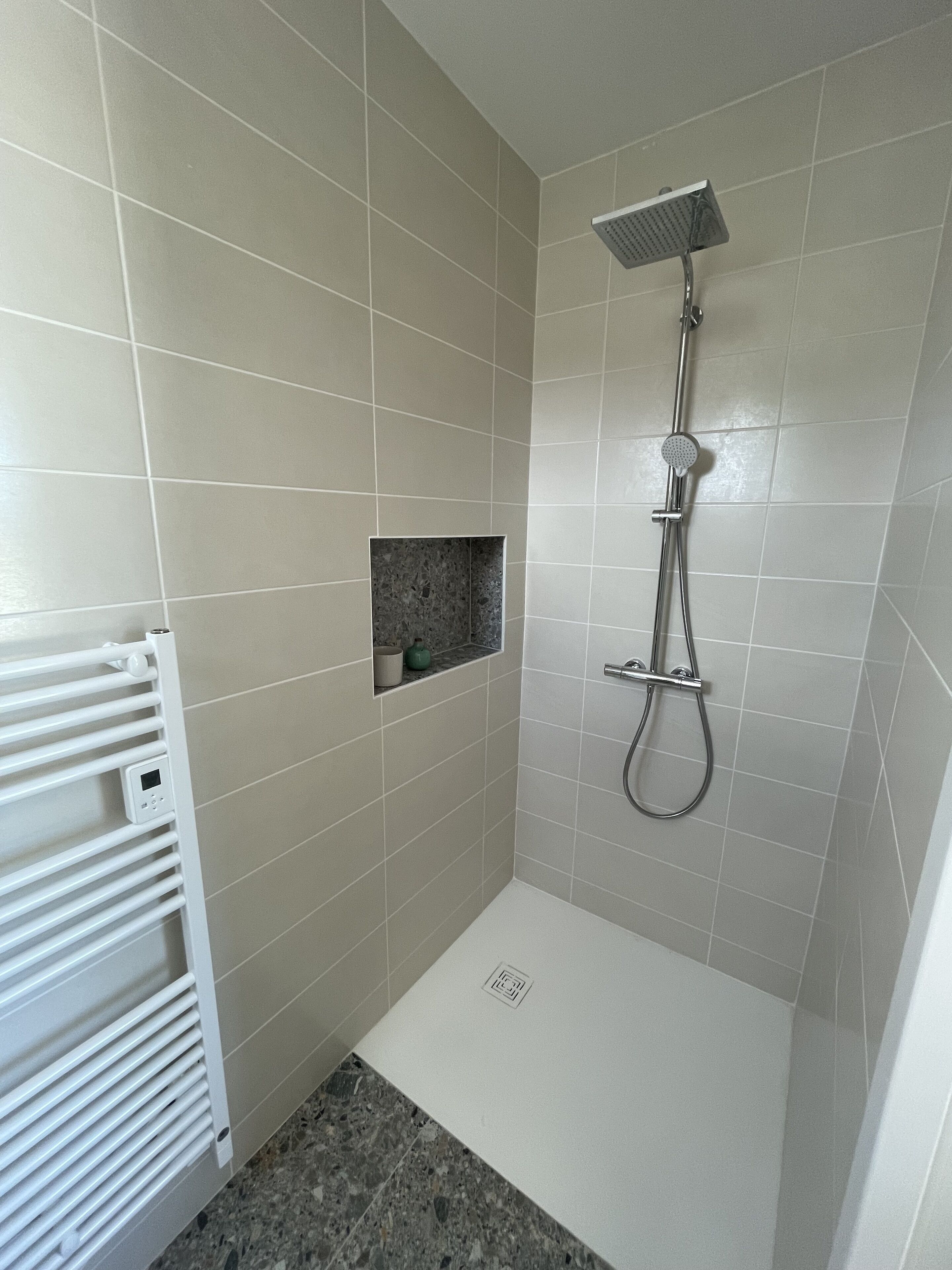 A small, modern shower room with a showerhead, a control panel, and a built-in shelf.