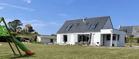 Une maison moderne avec un toit en pente, de grandes fenêtres et une cour gazonnée.