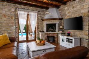 Een woonkamer met een stenen muur, een open haard, een televisie en uitzicht op een zwembad.