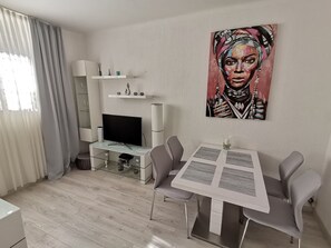 A modern living room with a flat-screen TV, a glass coffee table, and a dining area with two chairs. - Ana Center Apartment in the Center of Split City (Split)
