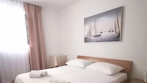 Een netjes opgemaakt bed met witte lakens en handdoeken, een houten hoofdbord, een nachtkastje met een lamp en een schilderij van zeilboten aan de muur.