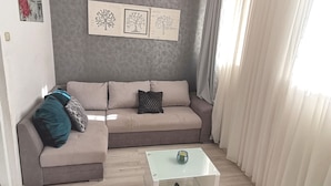 Een woonkamer met een beige bank, een glazen salontafel en een grijze accentmuur met illustraties van bomen.