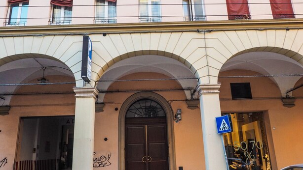 Ein Gebäude mit einem zentralen Eingang, mehreren Fenstern mit roten Vorhängen und einem Fußgängerübergang-Schild.