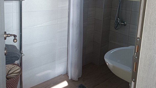 Uma casa de banho com chuveiro, pia e um porta-toalhas.