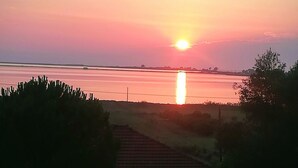 Atardecer sobre un cuerpo de agua, con una casa y una cerca en primer plano.