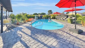 Ein Swimmingpool mit Ziegelterrasse, Liegestühlen und roten Sonnenschirmen.