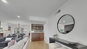 Ein modernes Wohnzimmer mit einer Couch, Hocker, einem Essbereich und einer Küche im Hintergrund.
