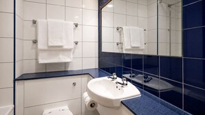 Un baño moderno con azulejos blancos, encimera azul, lavabo blanco, un espejo y una ducha.