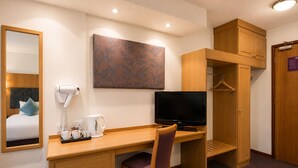 Habitación de hotel con un escritorio de madera, televisor, espejo, cafetera y armario.