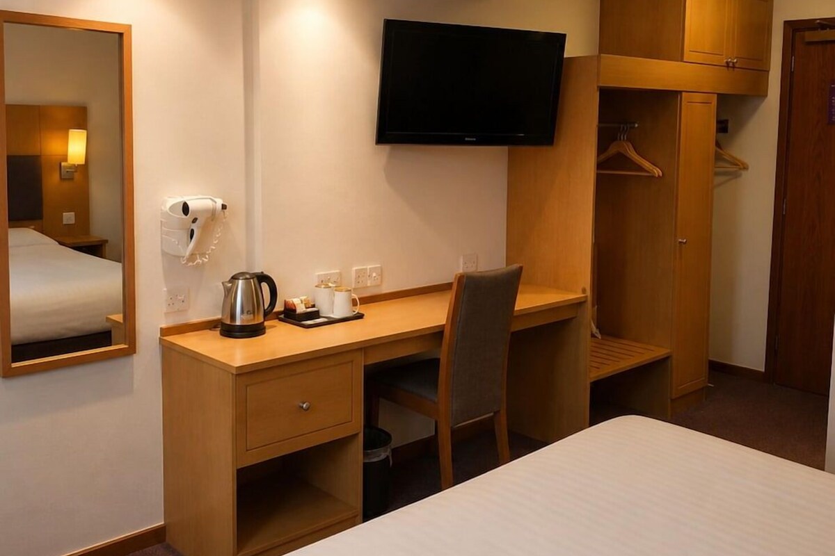 A hotel room with a bed, a desk with a chair, a television mounted on the wall, a coat closet, and a mirror.