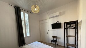 A bedroom with a bed, a hanging light fixture, a TV mounted on the wall, and a door. - Appartement T3 en Centre Ville a 5 Minutes de la Plage (Saint-Raphaël)