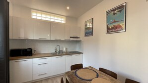 A modern kitchen with white cabinets, a microwave, and a sink. There is a dining table with chairs and two framed pictures on the wall. - Appartement T3 en Centre Ville a 5 Minutes de la Plage (Saint-Raphaël)