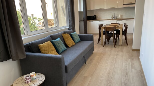 A modern living room with a grey sofa, a small round table with two patterned mugs, and a dining area with wooden chairs and a table. - Appartement T3 en Centre Ville a 5 Minutes de la Plage (Saint-Raphaël)