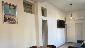 A dining area with a wooden table and chairs, a mounted TV, and a sofa in the living area. - Appartement T3 en Centre Ville a 5 Minutes de la Plage (Saint-Raphaël)