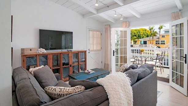 A living room with a sofa, a television, and a wooden cabinet. There is a glass door leading to an outdoor patio with a table and chairs.